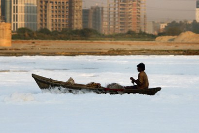 A dreadful warning: a fisherman paddles through a tide of toxic waste on the Yamuna river, against a backdrop of smog and high-rise construction