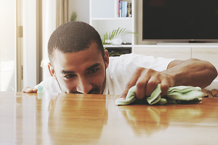 Shot of a focused young man cleaning the surface of a table with cleaning equipment at home during the day
