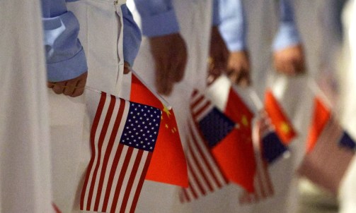 BEIJING, CHINA - MAY 13: Chinese youth hold American and Chinese flags as they join officials to welcome U.S. President Donald Trump at Beijing Capital International Airport on May 13, 2026 in Beijing, China. President Trump is meeting with President Xi Jinping in Beijing to address the Iran conflict, trade imbalances, and the Taiwan situation while establishing new bilateral boards for economic and AI oversight. (Photo by Alex Wong/Getty Images)